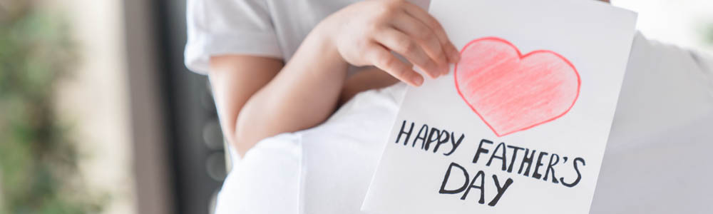 Close-up of child holding a Happy Father's Day card up in the arms of her dad